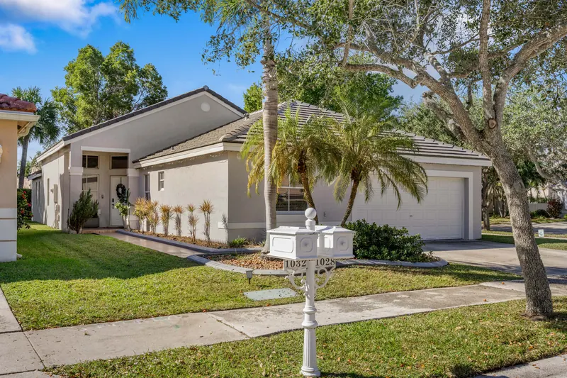 Single-story home with a driveway, palms and mature shade trees