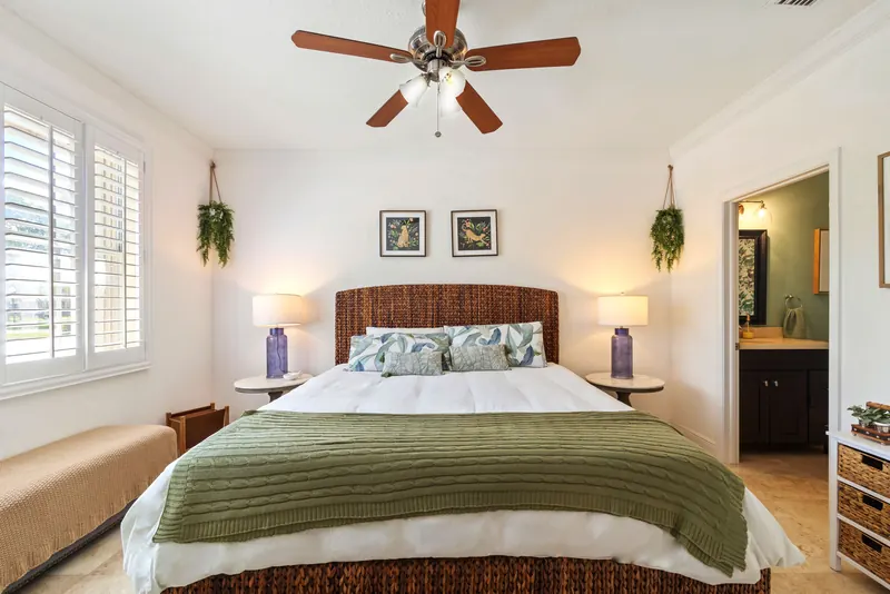 Bedroom with a woven headboard, green bedding and white shutters