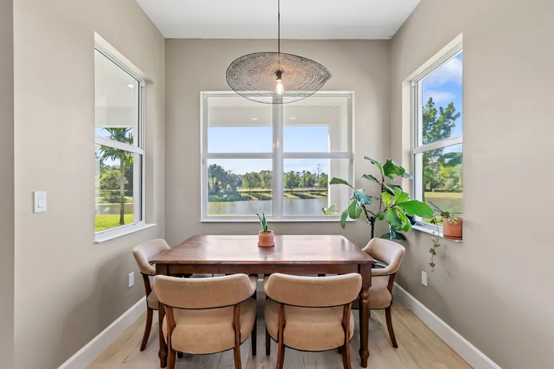 Dining nook with a wood table, woven chairs and windows overlooking a lake