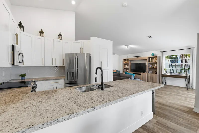 White kitchen with a stone-topped island and an open view into the living room