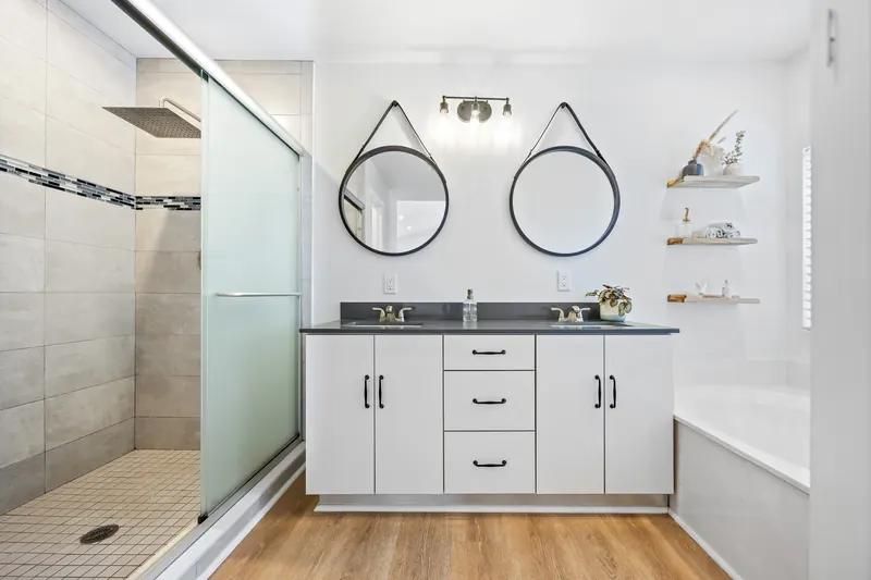 Double vanity with round mirrors, pale cabinets and open wall shelving