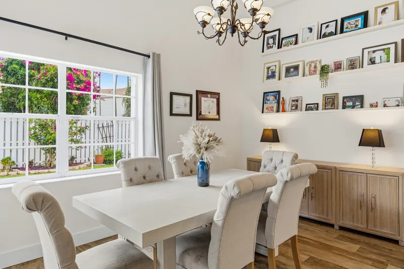 Dining table with upholstered chairs beside windows and white kitchen cabinets