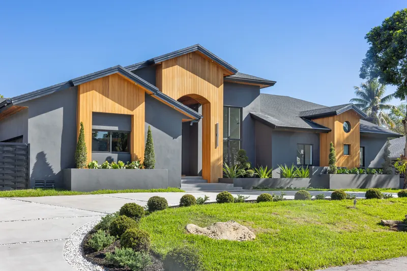 Front view of a charcoal-gray home with wood cladding, an arched entry and a landscaped lawn